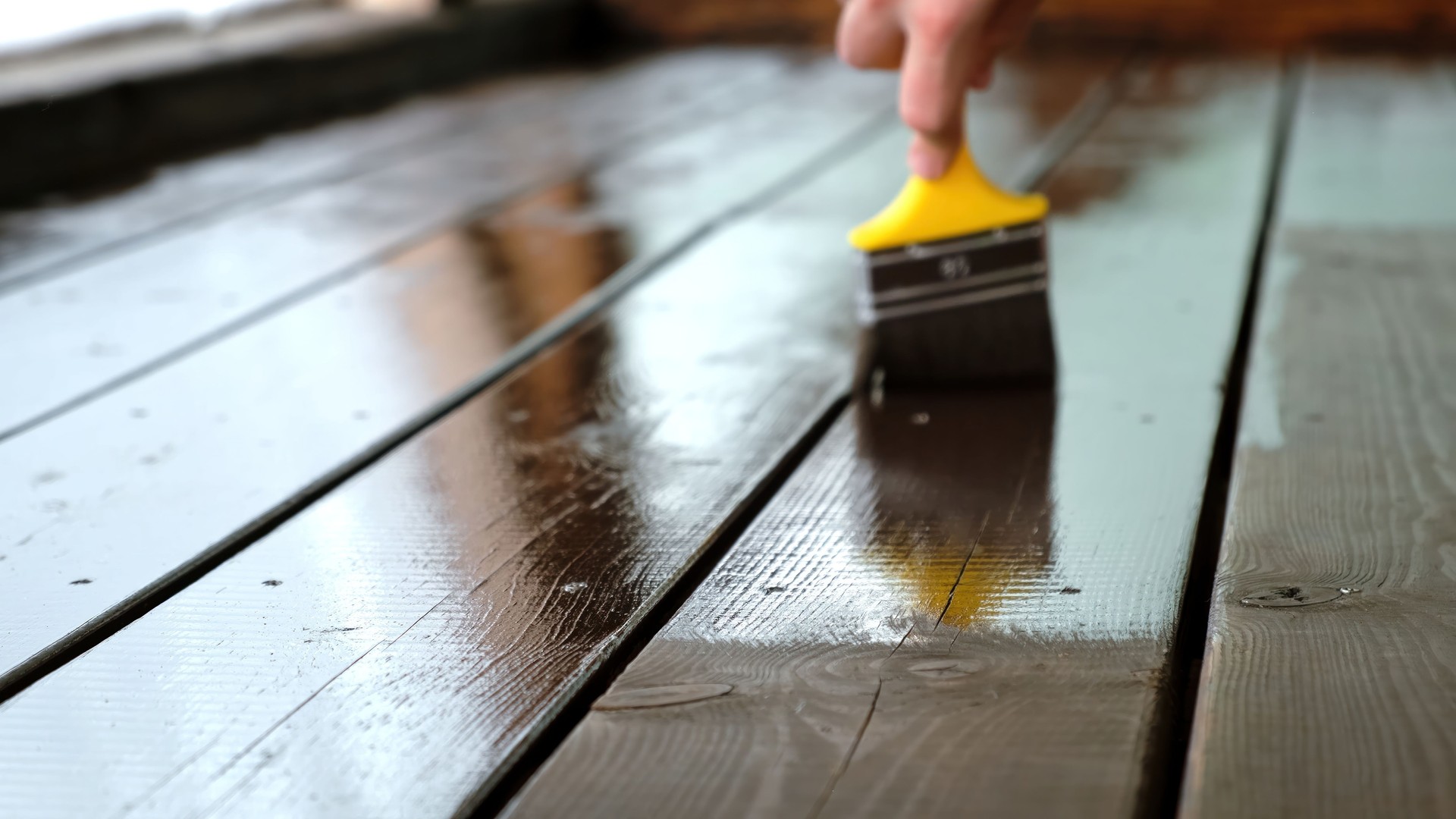 Close-up of a brush painting wood floor in brown color. Wood plank impregnation. Finish oil coating of board. Second layer of oiling. Manual construction work in a gazebo. Natural building materials
